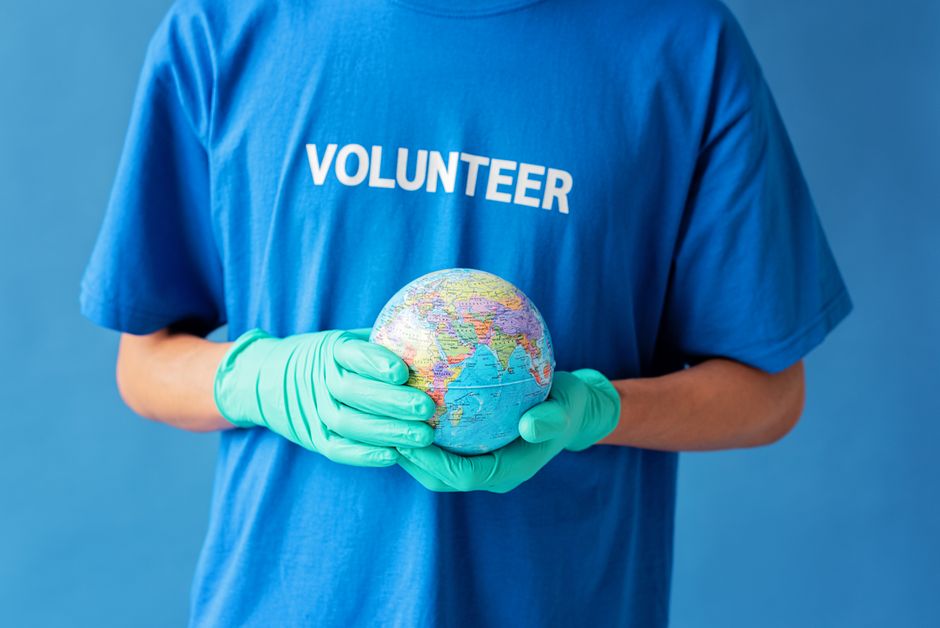 A volunteer in gloves holds a globe, symbolizing global environmental support.